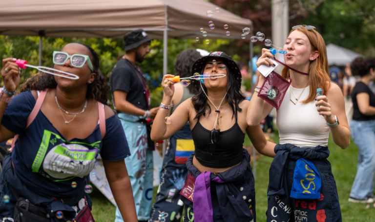 Student leaders wearing colourful rep suits and blowing bubbles at Welcome Week