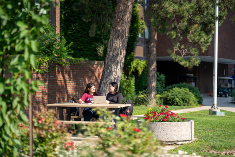 Two students sitting at a picnic table on campus during summer