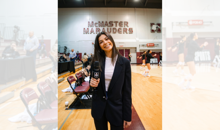 Student staff holding a mic on court at a volleyball game.