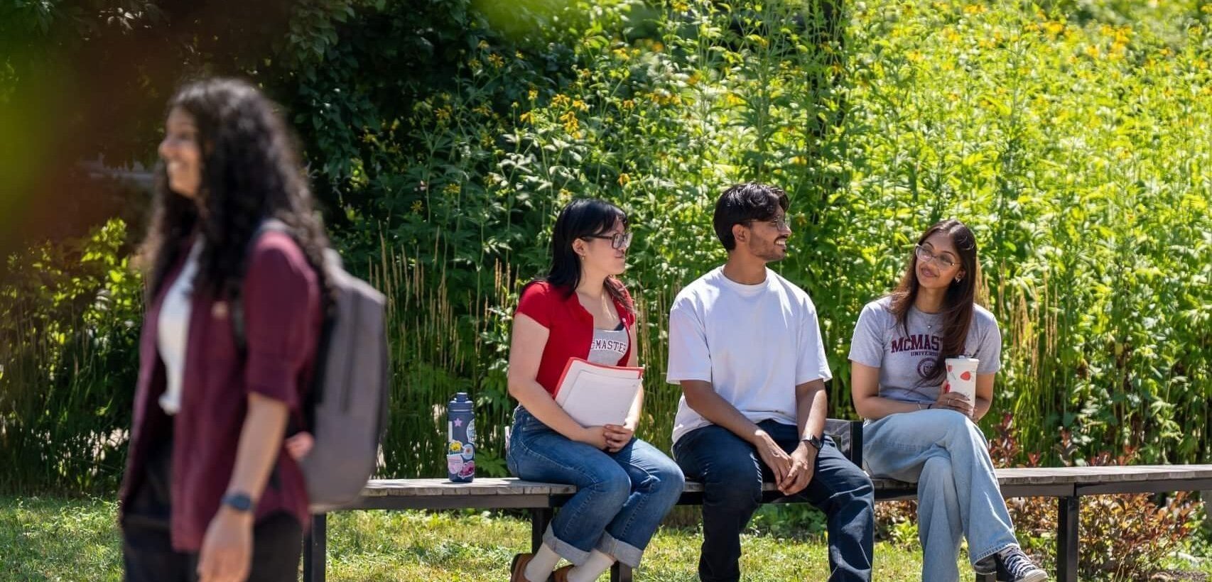 Students sitting on a bench while another student walks by on campus.