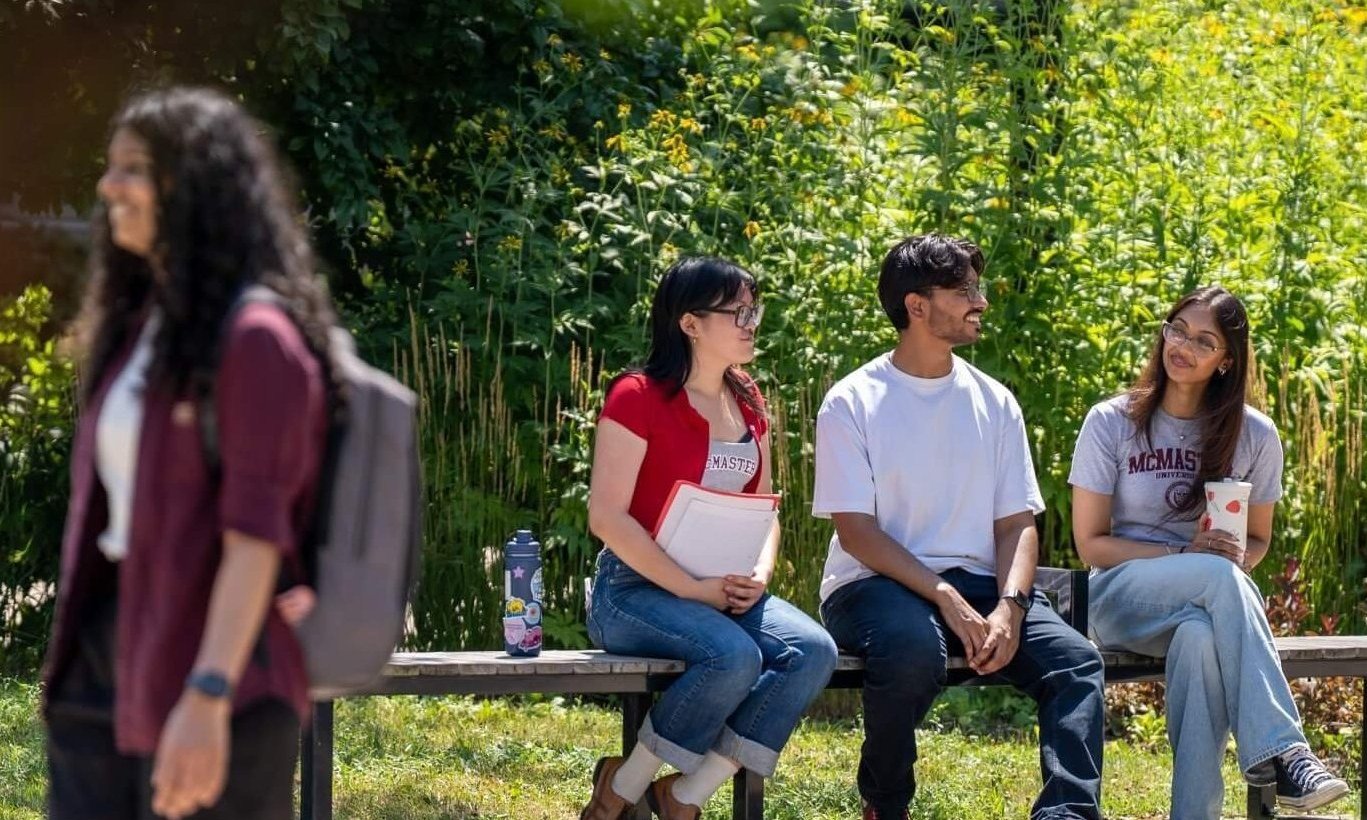 Students sitting on a bench while another student walks by on campus.