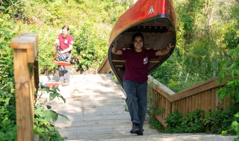 Student walking while carrying canoe.