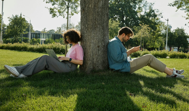 Two people sitting and reading by a tree.