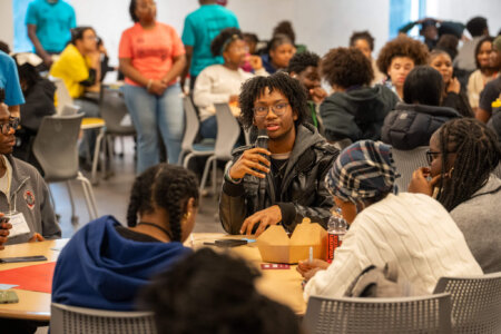 Student holding mic during event with full room of peers